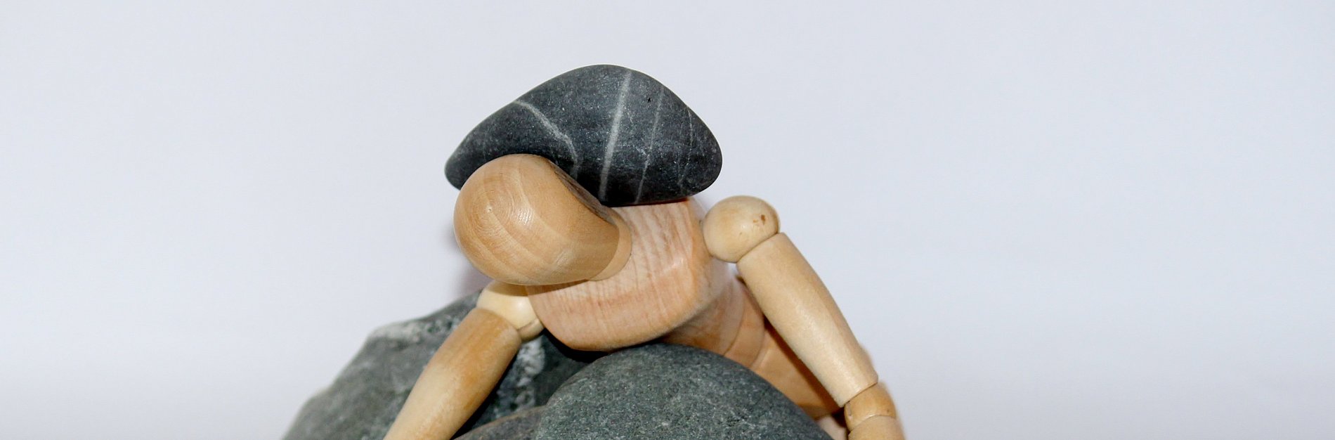 Ein Männchen aus Holz wird von dunklen Steinen niedergedrückt